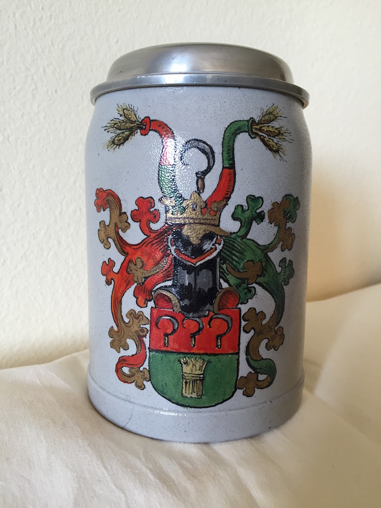 Bierkrug mit Deckel und aufgemaltem Wappen.